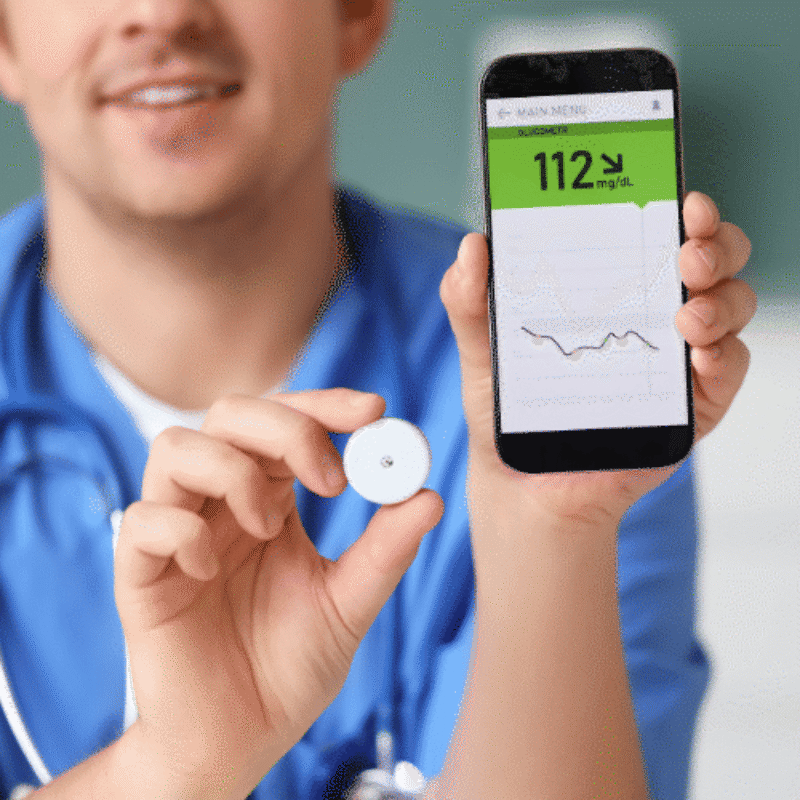 Doctor in scrubs holding up a sensor and a smartphone with numbers and a graph