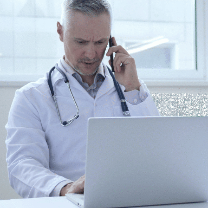 Doctor on phone and laptop with serious expression