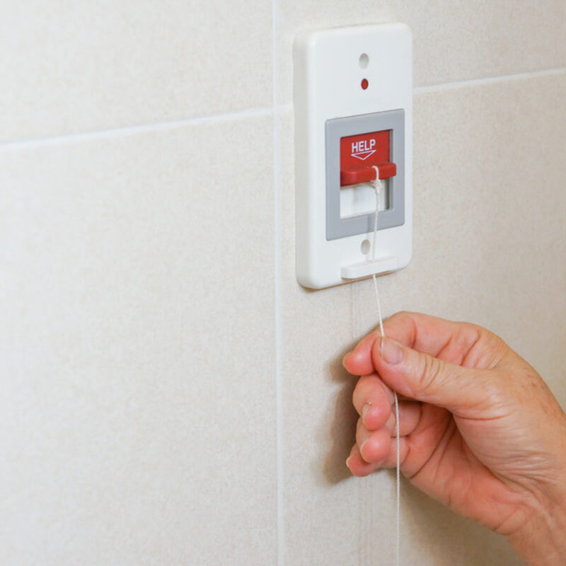 Hand pulling cord on fixed duress alarm marked help