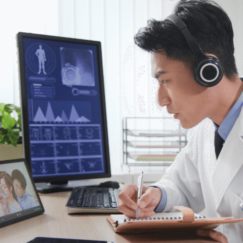 Male doctor in headphones using desktop and tablet computer