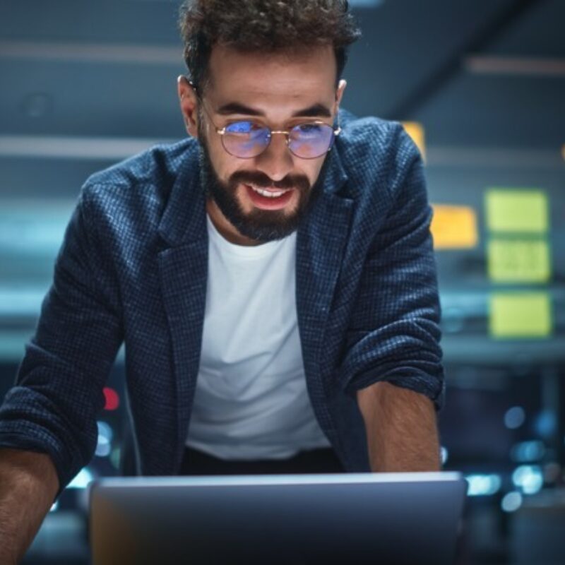 Man with beard and glasses looking at laptop in modern office