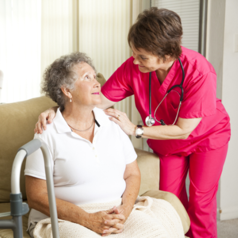 Nurse in pink scrubs comforting seated elderly patient