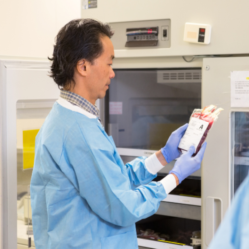 Technician in PPE removing blood bag from refrigerator