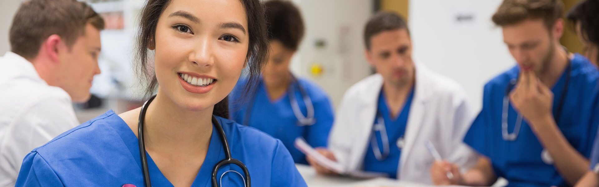 Female doctor in scrubs sitting at desk with team