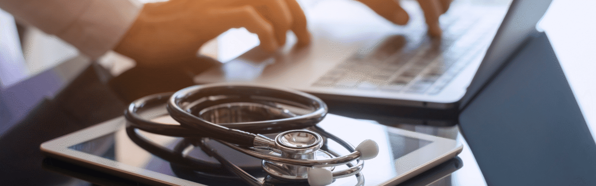 Stethoscope on tablet pc with laptop in use behind