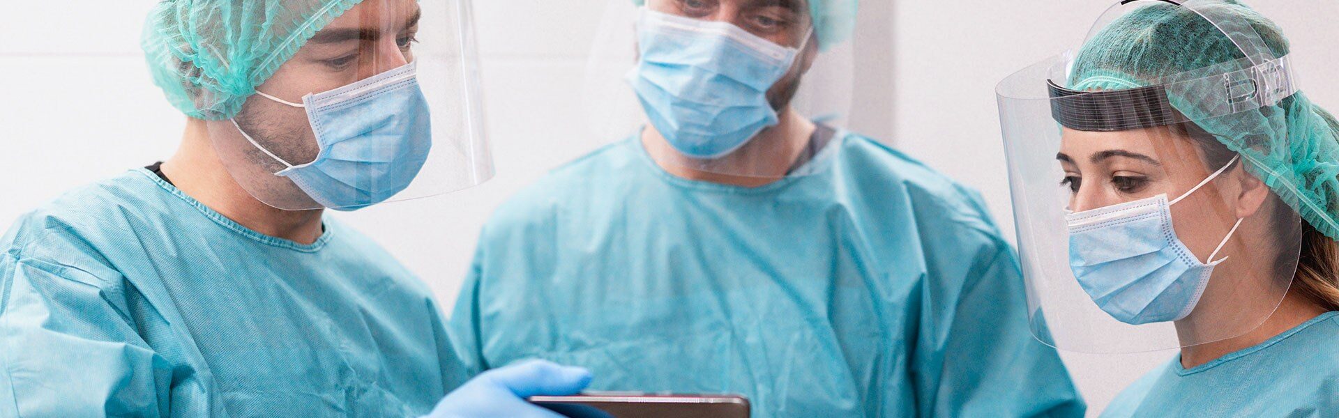 Three doctors in scrubs and masks looking at a mobile phone